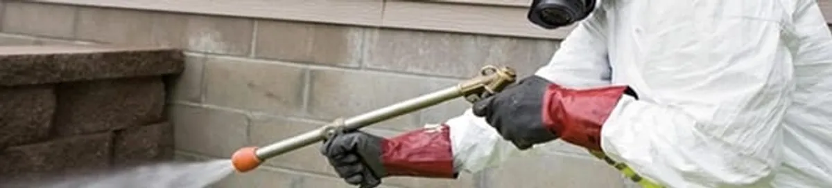 Pest control technician applying exterior insect treatment along a home foundation in Cambridge, MA