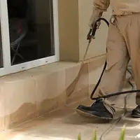 General pest control technician spraying exterior perimeter around a home in Cambridge, MA