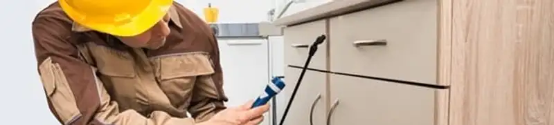 Roach exterminator applying treatment under kitchen cabinets in Cambridge, MA