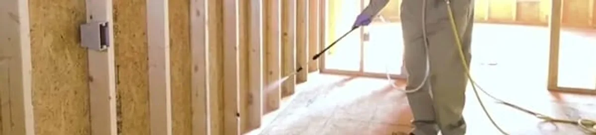 Termite treatment technician applying spray along framing and unfinished walls in Cambridge, MA